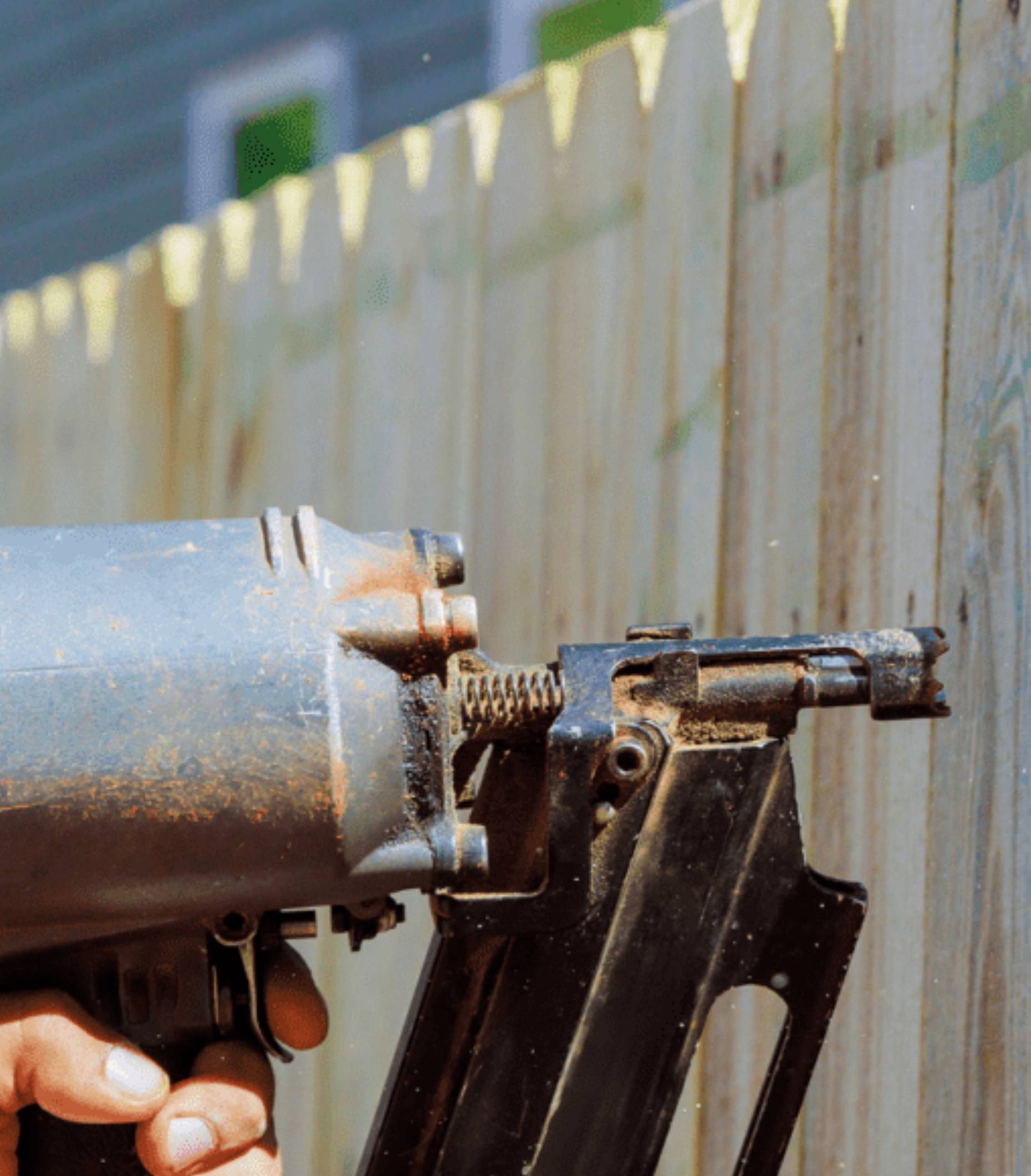 A close-up of a nail gun being used against a wooden fence.