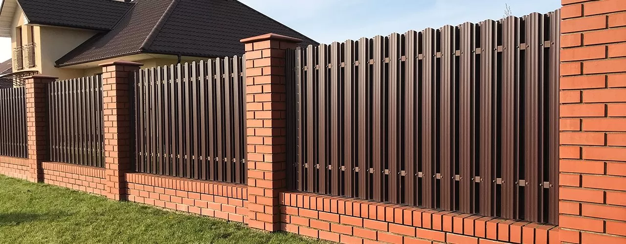 Modern metal and brick fence with vertical slats and pillars.