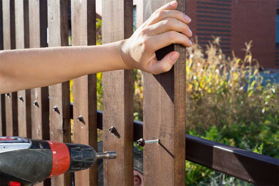A person fixing a wooden fence post with a power drill outdoors.