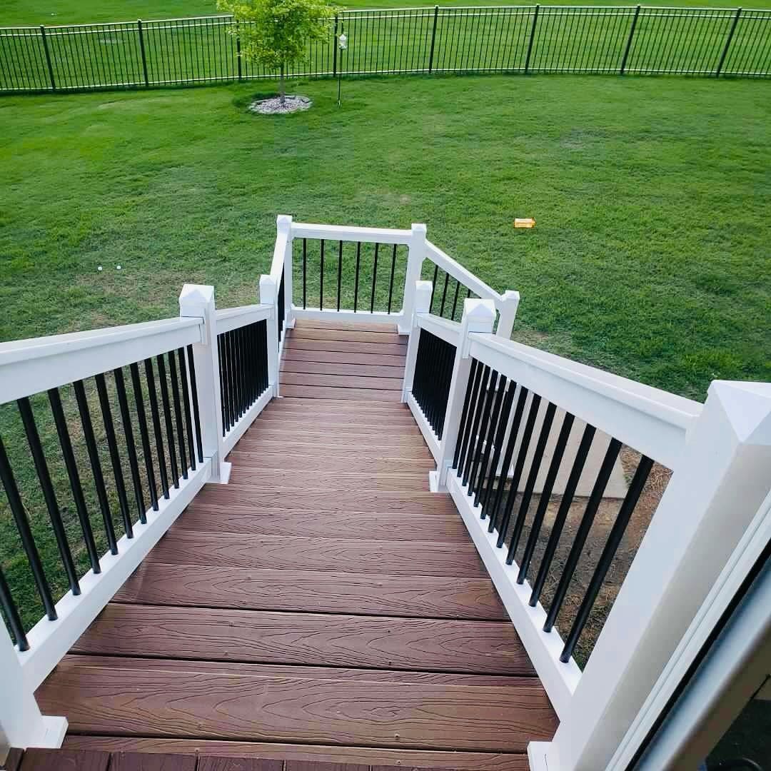 Wooden staircase with white railings leading to a green lawn.