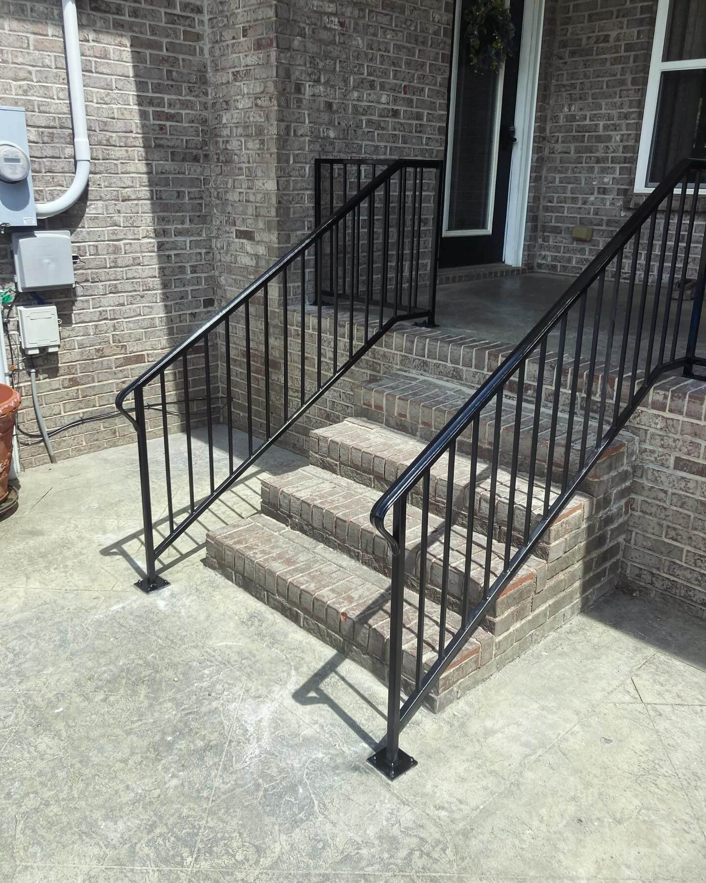 Black metal handrails installed on concrete stairs outside a brick building.
