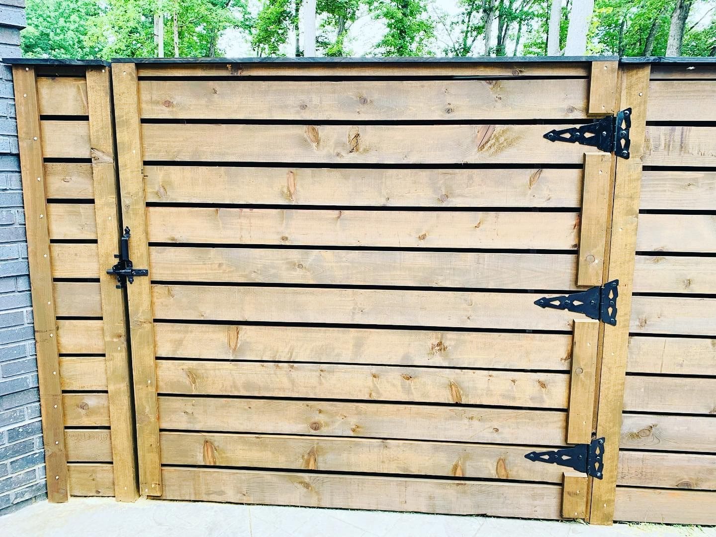 Wooden gate with metal hinges in a forest setting.